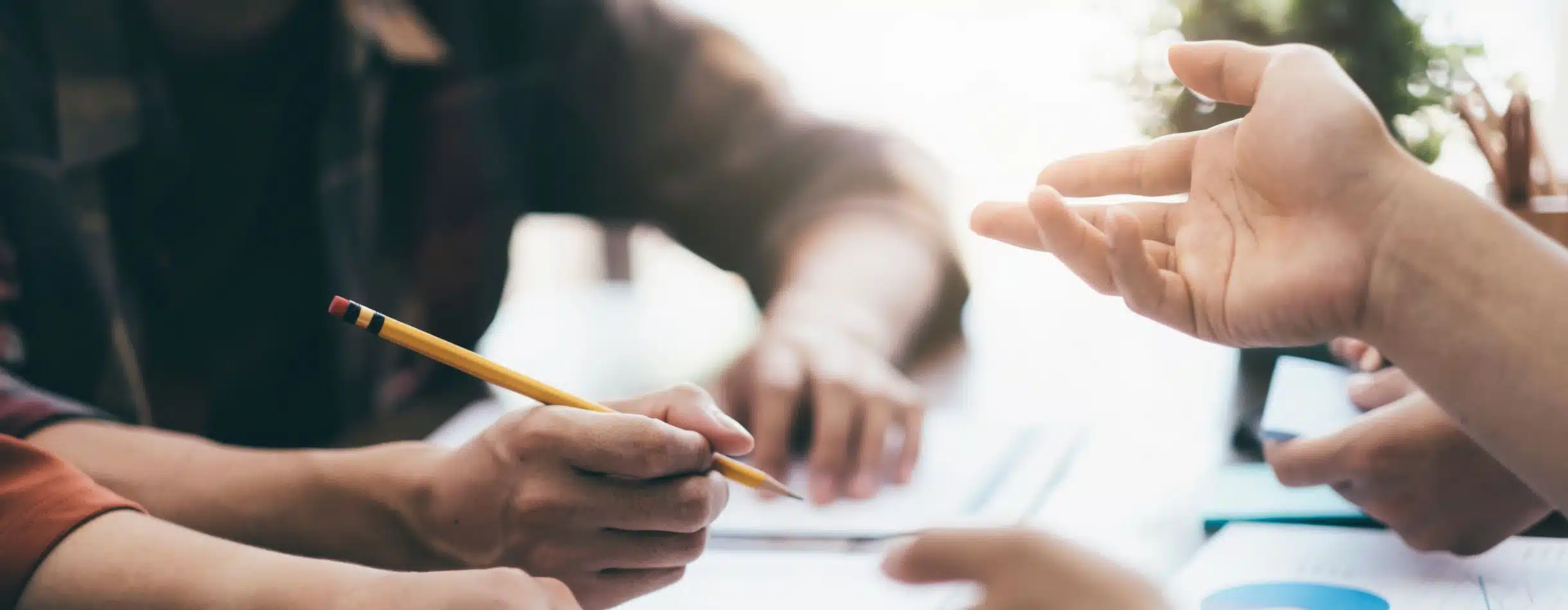 Two colleagues are having a discussion. One extends out their hand to emphasize a point while the other person jots notes down with a pencil on a lined notebook.