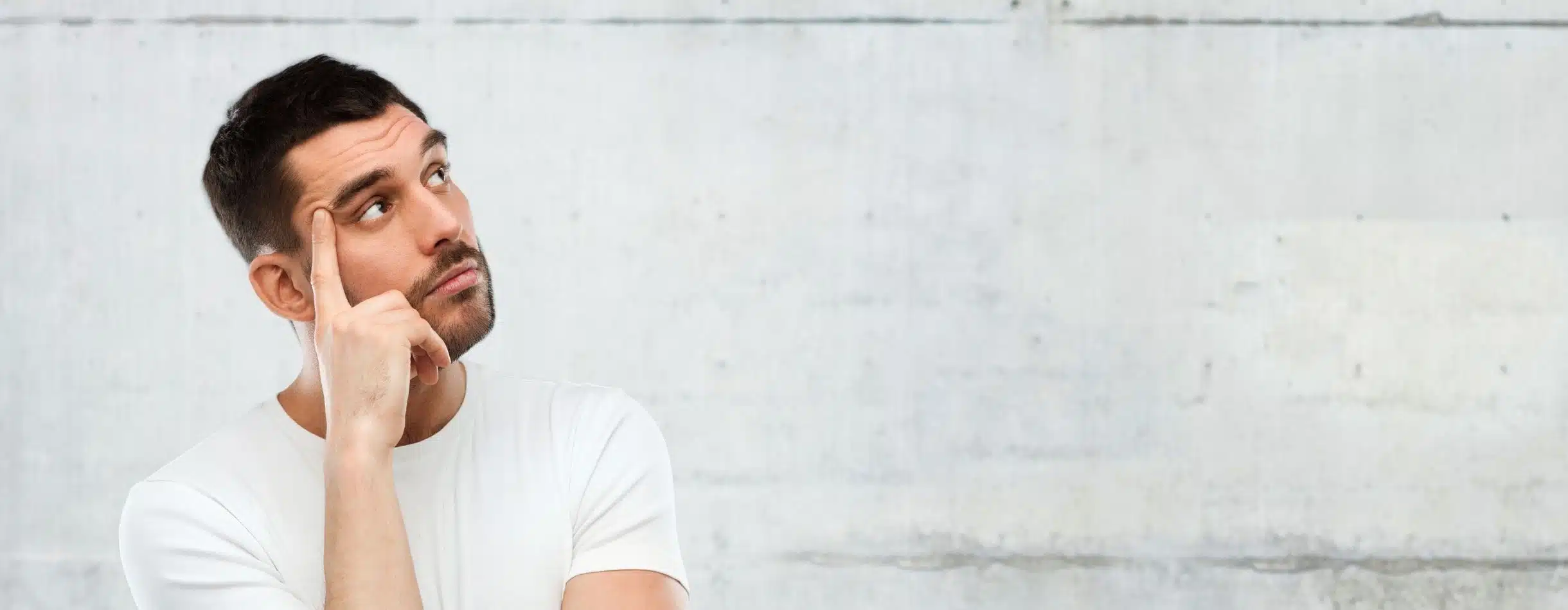 A man is thinking as he looks towards the ceiling of the room with his arm resting on his face with the index finger nestled near his forehead.