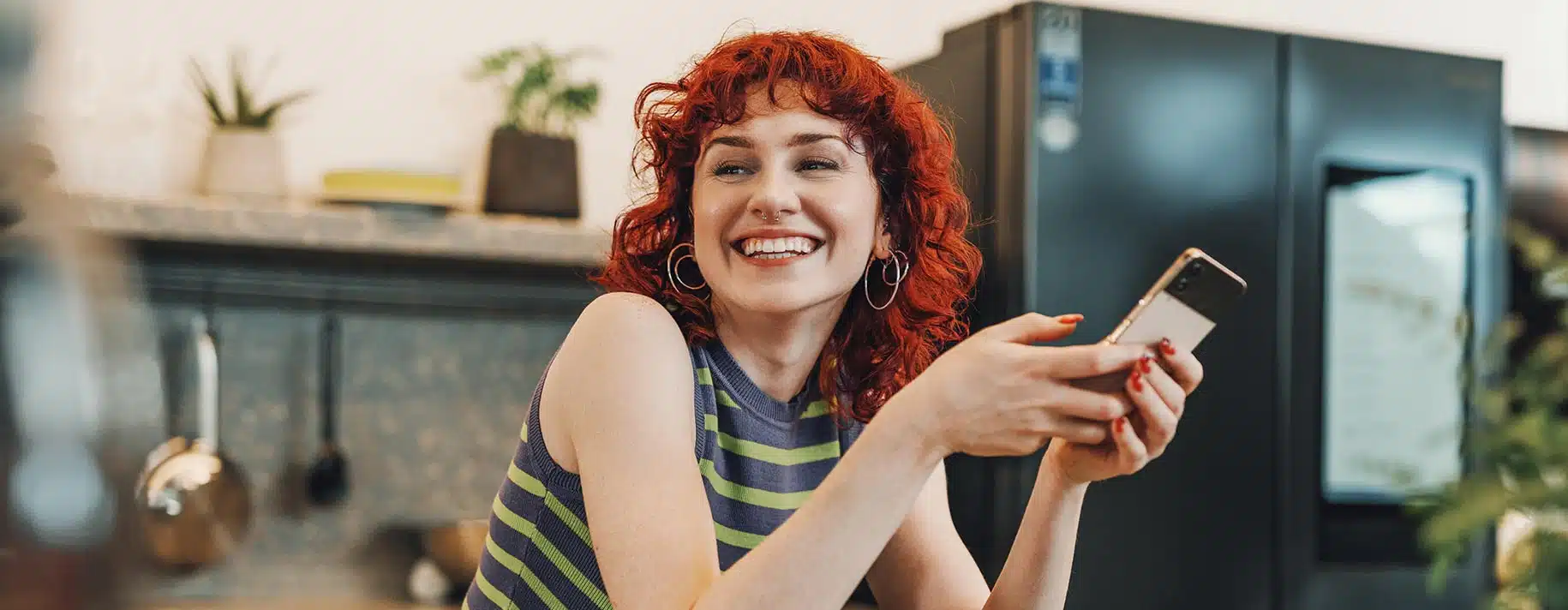 A woman smiling while on her phone sitting in a kitchen.