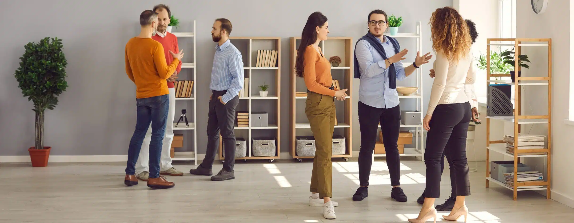A group of people are participating in one-off conversations between one another in a grey, modern room with adequate natural lighting.