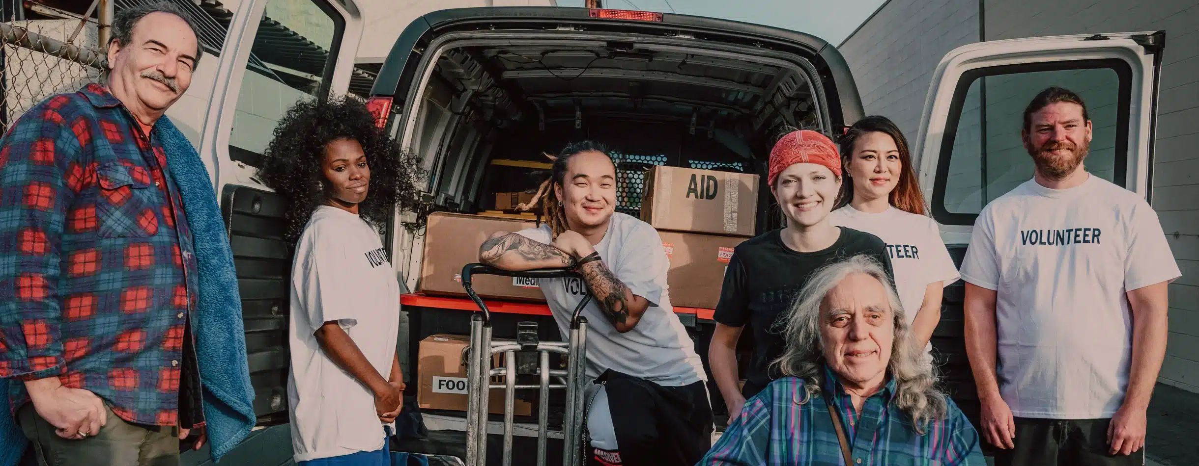A group of people stand proudly posing for a group photo after loading a van with boxes of food, aid, and supplies.