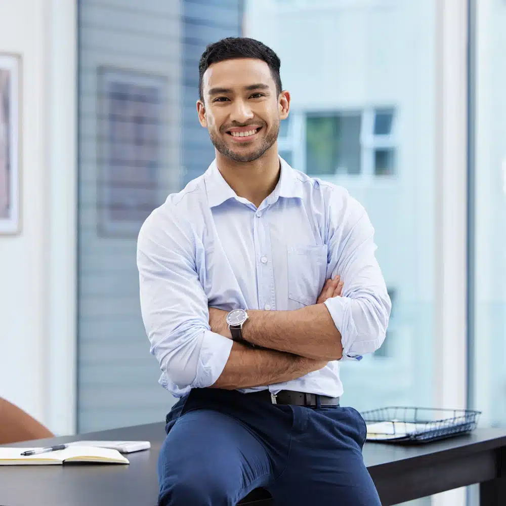 I Call The Shots Around Here. Shot Of A Handsome Young Businessman Sitting On His Desk In The Office With His Arms Folded.
