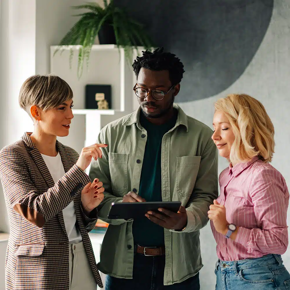 Two women and a man work together and collaborate on tablet.