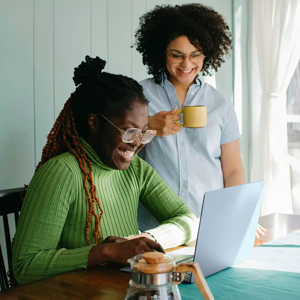 Two woman at table smiling at computer